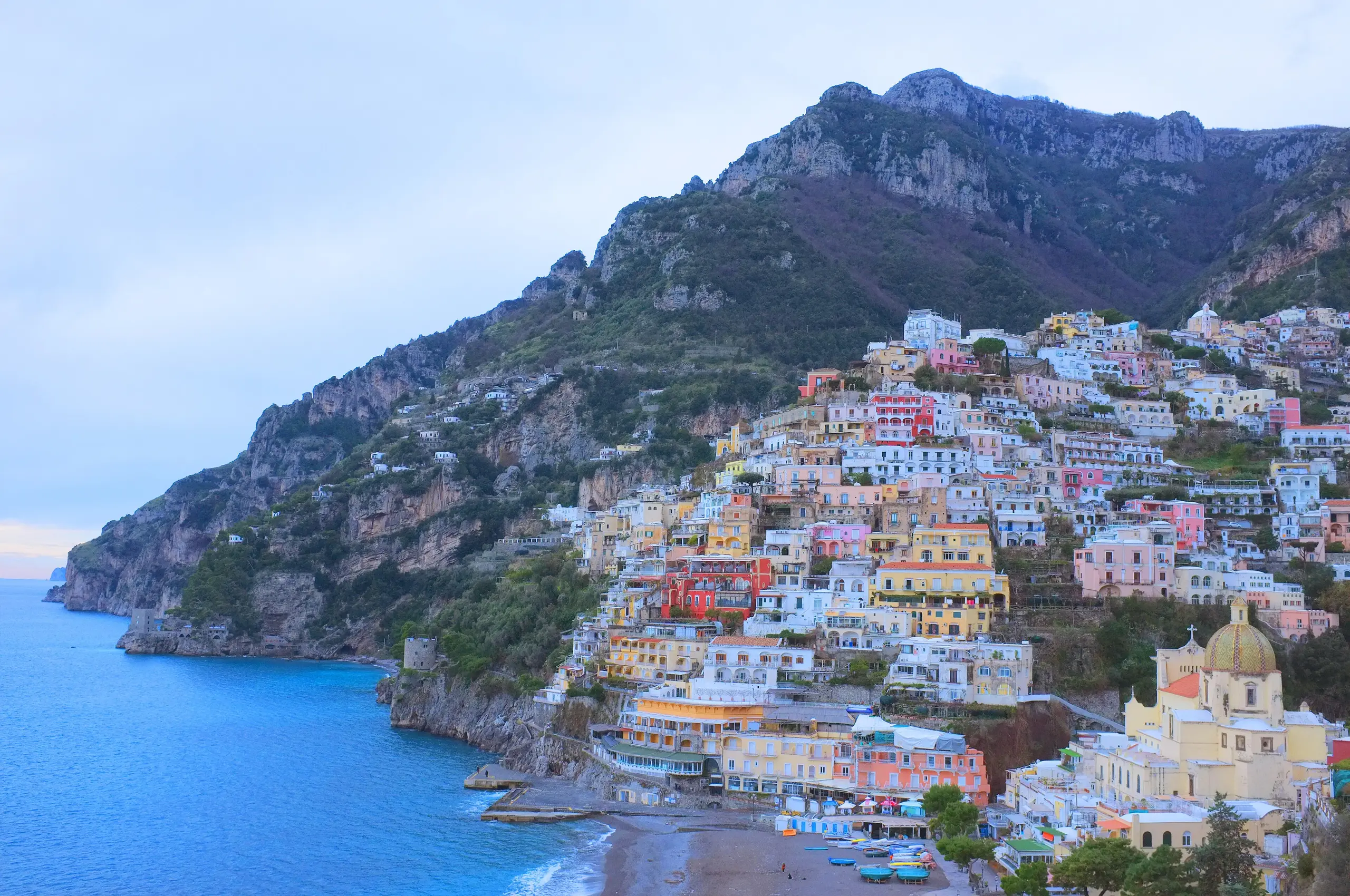 Positano's pastel houses stacked up a steep hillside above the sea in soft evening light.